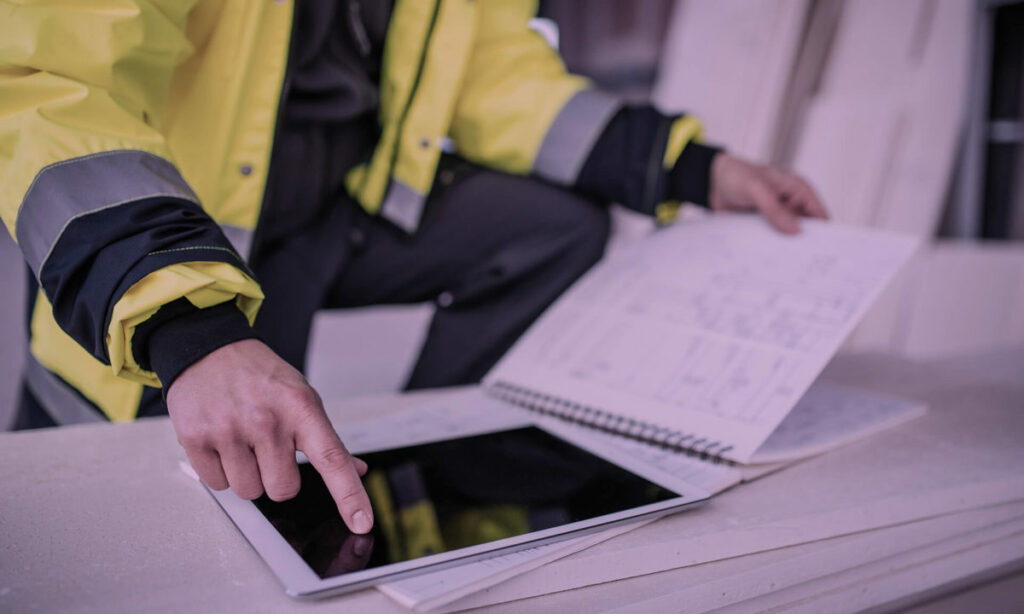 Person i refleksjakke som sammenligner en ipad og en fysisk bok