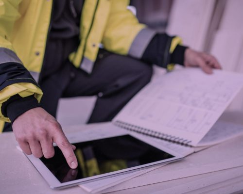 Person i refleksjakke som sammenligner en ipad og en fysisk bok