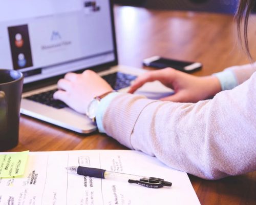 Person som jobber på pc med en fysisk sjekkliste og kopp te